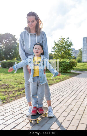 Young happy family smiling réjouissance, trains mom petit garçon 3-5 ans, l'enfant apprend premières leçons skate scooter, équilibre, détente, l'été jour d'automne Banque D'Images