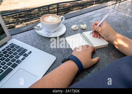 Femme écrit à côté de l'ordinateur portable ordinateur et tasse de cappuccino Banque D'Images