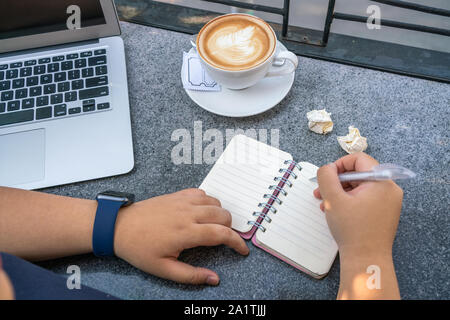 Woman writing notes next to laptop et tasse de Cappuccino chaud Banque D'Images