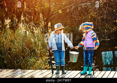 Deux petites filles avec des cannes à pêche, ils sont debout sur un ponton en bois et regarder les poissons capturés dans un seau. Banque D'Images