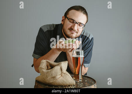 Confiant avec brasseur de bière en verre auto conçu dans le tonneau en bois sur fond gris. Propriétaire d'usine présente ses produits de la brasserie, à tester sa qualité. La bière, boisson, l'alcool. Banque D'Images