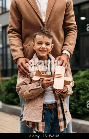 Vue partielle de père en fils et robe élégante smiling holding toy plane on street Banque D'Images