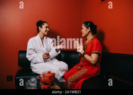Jolie femme en peignoir et asiatiques en conversation masseur spa Banque D'Images