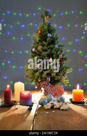 Arbre de Noël entouré par les bougies, les cookies et les oeufs avec rétro-éclairage sur la table Banque D'Images