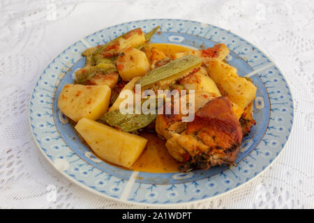 Une authentique Assiette de poulet au four crétois avec des pommes de terre et courgettes (zuccini) dans une riche sauce tomate et sauce d'huile d'olive aux herbes Banque D'Images