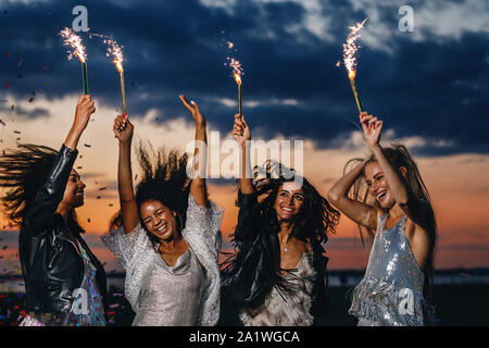 Quatre heureux amis féminins avec des cierges. Les femmes élégantes dancing au coucher du soleil. Banque D'Images