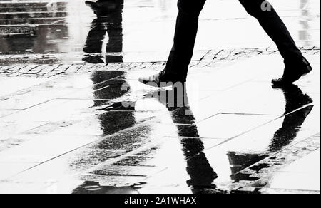 Silhouette et la réflexion d'un homme en marche chaussures élégante rue ville humide sur s jour pluvieux, les jambes en noir et blanc Banque D'Images