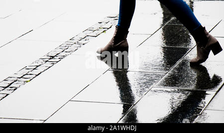 Ombre Silhouette et la réflexion d'une femme à la cheville chaussures de démarrage humide marche ville rue un jour de pluie, les jambes seulement Banque D'Images