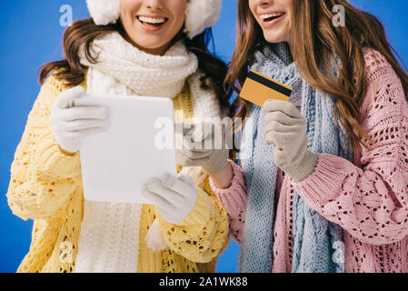 Portrait of smiling women dans pulls et écharpes holding digital tablet et isolé de carte de crédit sur bleu Banque D'Images