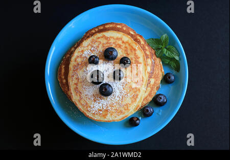Pile de crêpes maison sur plaque bleu turquoise avec des bleuets et saupoudrés de sucre glace. Fond sombre. Vue d'en haut Banque D'Images