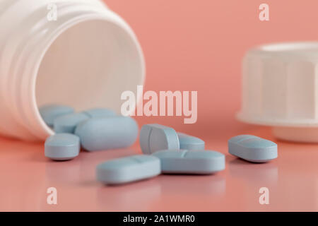 White flacon de médicaments et pilules bleues sur fond rose. Close-up. Banque D'Images