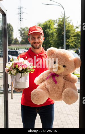 Livraison positive man holding teddy bear et de fleurs Banque D'Images