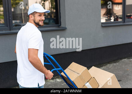 Livraison barbu souriant homme debout avec livraison panier près du bâtiment Banque D'Images