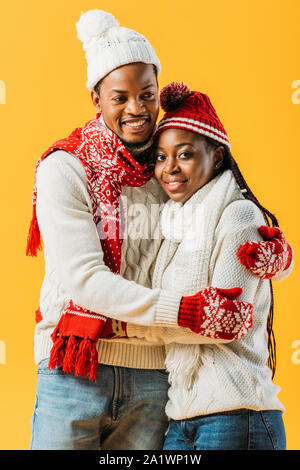 African American couple en tenue d'hiver douillet à la caméra et à étreindre l'autre isolé sur le jaune Banque D'Images