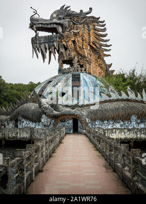 Immense et effrayant dragon en pierre de pointes et bouche ouverte avec dents en vue de profil avec sentier au parc aquatique abandonné, Thuy Tien lake, Hue, Vietnam Banque D'Images