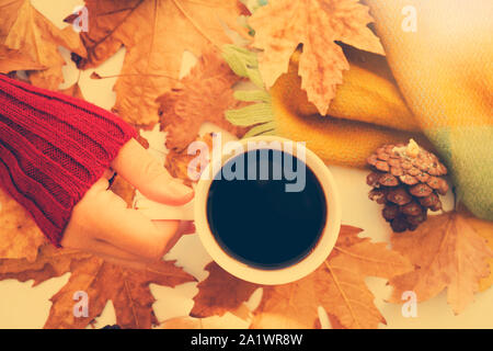 Les mains tenant café noir chaud, la couverture et les feuilles d'automne sur fond blanc. Vintage tonifiant. Détendez-vous d'automne concept Banque D'Images