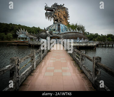 Immense et effrayant dragon en pierre de pointes et bouche ouverte avec dents en vue de profil avec sentier au parc aquatique abandonné, Thuy Tien lake, Hue, Vietnam Banque D'Images