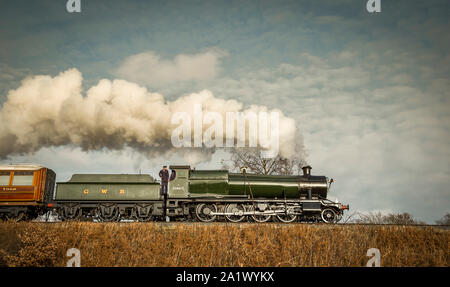 Vue latérale à angle bas d'un train à vapeur britannique d'époque se déplaçant le long de la voie ferrée dans une ambiance lumineuse de campagne d'hiver. Train de vapeur de locomotive. Banque D'Images