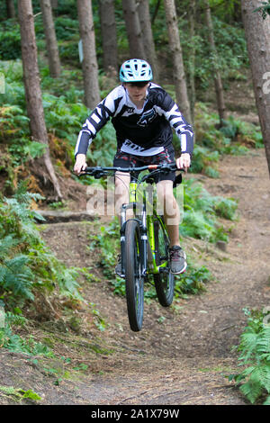 Teenage boy leaping autour sur un vélo de montagne sur Kinver Edge piste en forêt entouré de grands pins. Banque D'Images