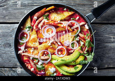 Chilaquiles avec jambon, fromage panela émietté, tranches d'avocat et salsa de tomates dans une poêle sur une table en bois rustique, la cuisine mexicaine, vue horizontale Banque D'Images