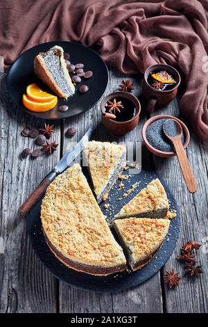 Graines de pavot Gâteau au fromage délicieux Crumble en tranches sur une plaque de pierre noire avec des tasses de café, le couteau et le tissu marron sur une table en bois rustique, vertical vi Banque D'Images