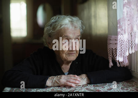 Vieille Femme aux cheveux gris et regarde par la fenêtre. Banque D'Images