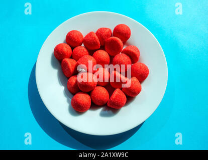 Bonbons sucrés fraise rouge en plaque blanche isolé sur fond bleu turquoise Banque D'Images