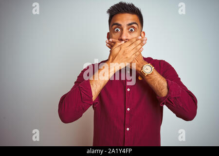 Jeune Indien man wearing red shirt debout sur fond gris isolé choqué couvrant la bouche avec les mains pour l'erreur. Concept Secret. Banque D'Images