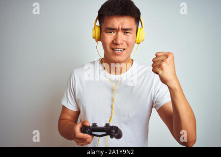 Les jeunes Chinois asiatique gamer man playing video game debout sur fond blanc isolé contrarié et frustré de crier avec colère, fou et crier Banque D'Images