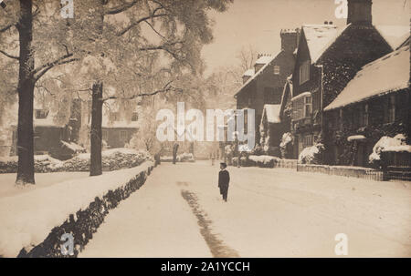 Vintage Edwardian Carte postale photographique de un village ou une ville recouverte de neige. Écolier se tenait dans la rue regarder les arbres. Banque D'Images