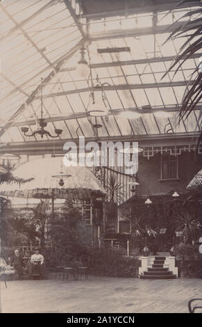 Vintage Début xxe siècle Carte postale photographique montrant un couple assis à une table sous un grand parasol à l'intérieur d'un pavillon au toit de verre. Banque D'Images