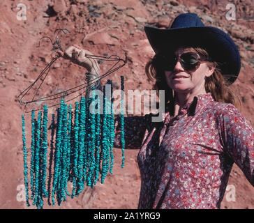 Une femme portant un chapeau de cowboy et de grandes lunettes de soleil contient jusqu'cintres de fil pour afficher des chaînes de petites billes de turquoise, elle vend aux touristes qui s'arrêtent le long d'une route dans le sud-ouest de l'Arizona, USA. L'opaque, bleu-à-vert pierre semi-officielle de l'Etat a été désigné le joyau de l'Arizona en 1974. Les Indiens Navajo et d'autres Amérindiens de la sud-ouest des États-Unis sont célèbres pour l'aide à créer des bijoux turquoise unique et à la mode, les articles qui vont de colliers, bracelets et boucles d'oreilles pour bracelets et boucles de ceinture. Banque D'Images