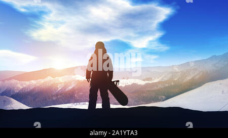 Contre les sommets enneigés des montagnes se dresse une silhouette sombre d'un snowboarder. Banque D'Images