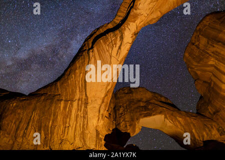 À la recherche jusqu'à l'emblématique arc double allumé contre un rempli d'étoiles Voie Lactée dans Parc National Arches dans Moab, Utah. Banque D'Images