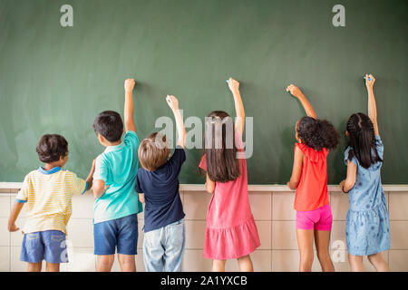 Groupe multi-ethnique de l'école des enfants s'appuyant sur le tableau Banque D'Images