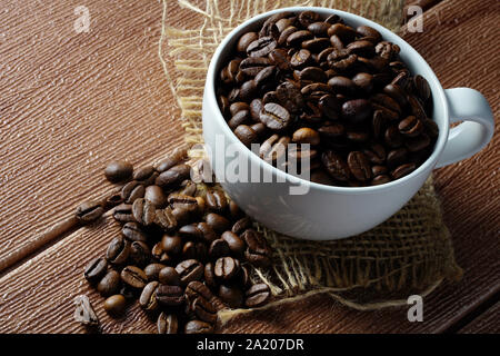 Grains de café dans une tasse blanche vide et sacs sur une table en bois Banque D'Images