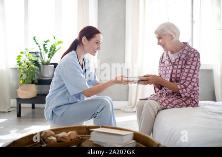 Caring nurse smiling tout en donnant au livre de femme Banque D'Images