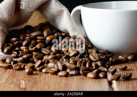 Grains de café dans une tasse blanche vide et sacs sur une table en bois Banque D'Images