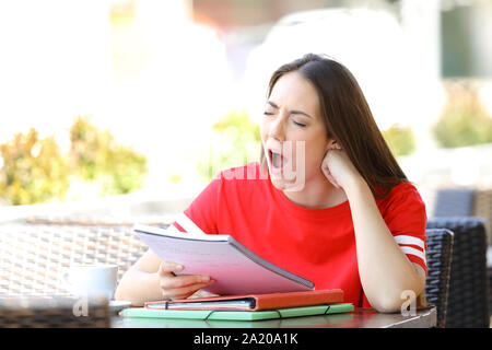 Bored student yawning holding note étudiant dans un bar terrasse Banque D'Images