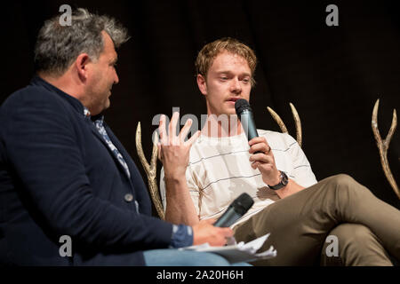 27 septembre 2019, Basse-Saxe, Langenhagen : l'acteur britannique Alfie Allen parle à un animateur de la 'Game of Thrones' tir à l 'événement ventilateur trône con' dans un hôtel à l'aéroport Hannover-Langenhagen. Selon les organisateurs, environ 800 fans sont venus pour être près de leurs idoles de la série. Photo : Moritz Frankenberg/dpa Banque D'Images