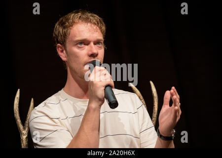 27 septembre 2019, Basse-Saxe, Langenhagen : l'acteur britannique Alfie Allen parle de la 'Game of Thrones' tir à l 'événement ventilateur trône con' dans un hôtel à l'aéroport Hannover-Langenhagen. Selon les organisateurs, environ 800 fans sont venus pour être près de leurs idoles de la série. Photo : Moritz Frankenberg/dpa Banque D'Images