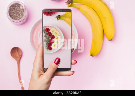 Woman's hand holding phone au-dessus de la table avec bol smoothie Banque D'Images