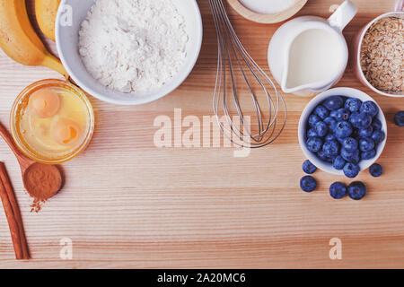 Ingrédients pour muffins aux bleuets préparation sur table en bois, vue du dessus. Banque D'Images
