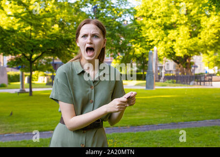 Jeune fille blonde indignés dans une robe verte avec une carte de crédit sur un arrière-plan du parc. Problèmes de la banque et de la résolution des problèmes. Antécédents de crédit Banque D'Images