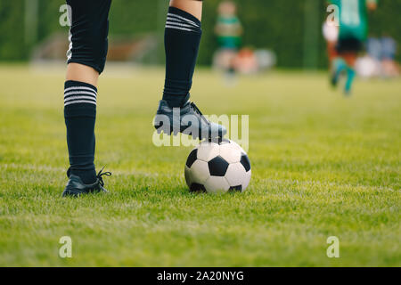 Un jeune joueur de football pour balle sur pelouse. Garçon dans un sport. Player vêtu de noir et chaussettes football soccer cleats. Horizontal Football cl Banque D'Images