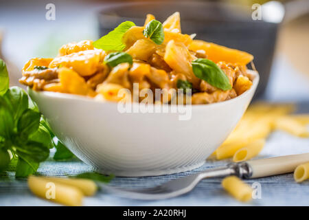 Les pâtes penne avec morceaux de poulet au basilic et parmesan champignons cuisine italienne dans un bol blanc sur la table de cuisine Banque D'Images