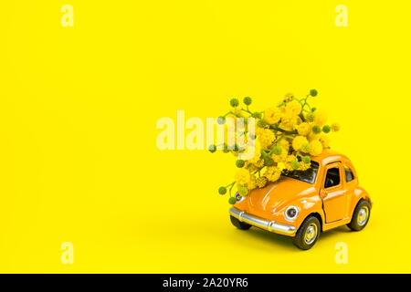 Moscou, Russie - le 23 février 2019 : 8 mars Journée internationale de la femme carte avec toy voiture rétro modèle de livrer bouquet de fleurs mimosa sur jaune Banque D'Images