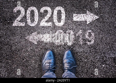 2020 et 2019 avec les flèches de direction écrit sur une route asphaltée, les jambes en arrière-plan Banque D'Images