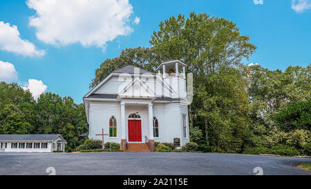 Petite église blanche avec porte rouge d'arbres sur une colline Banque D'Images