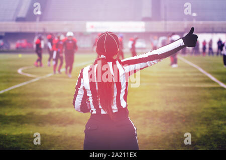 Vue arrière de l'arbitre de football américain féminin signaux donnant aux joueurs professionnels au cours de match sur le terrain du stade Banque D'Images